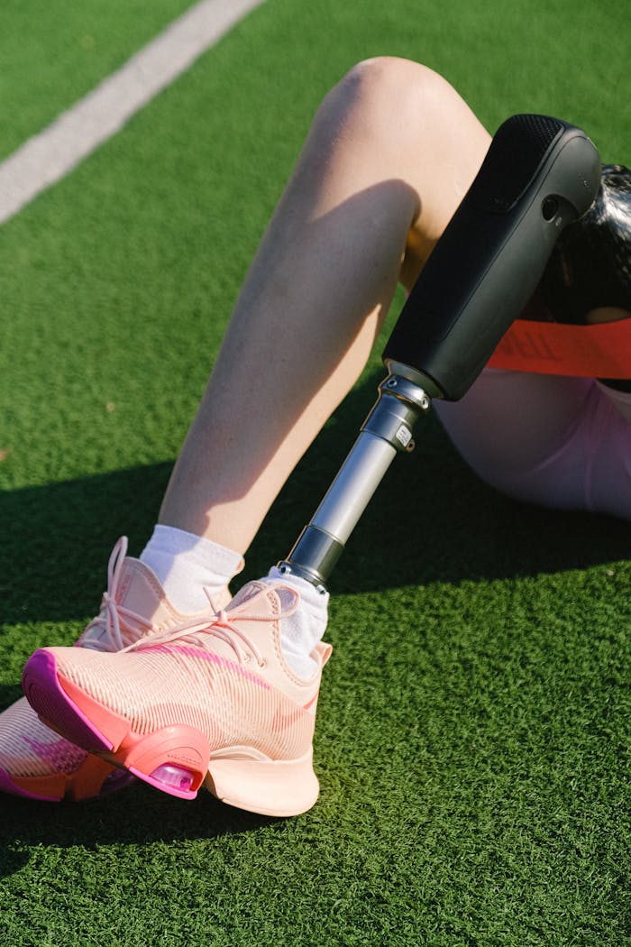 get-in-touch Close-up of a female athlete with a prosthetic leg resting on grass in bright sneakers.