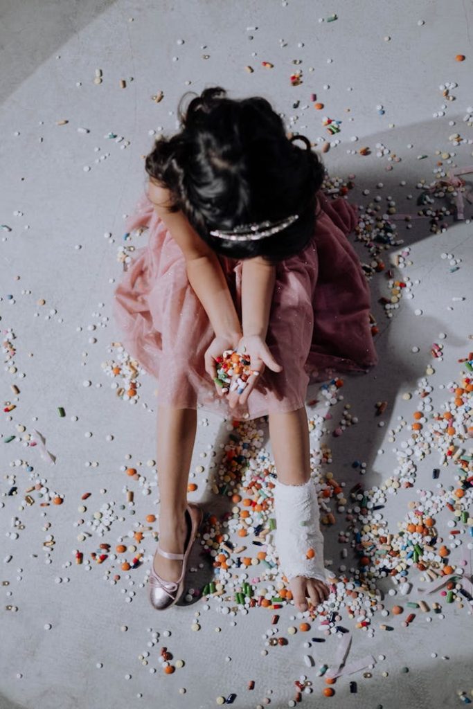 pexels photo 6191560 A young girl in a pink dress sits with an orthopedic cast surrounded by various pills and capsules.